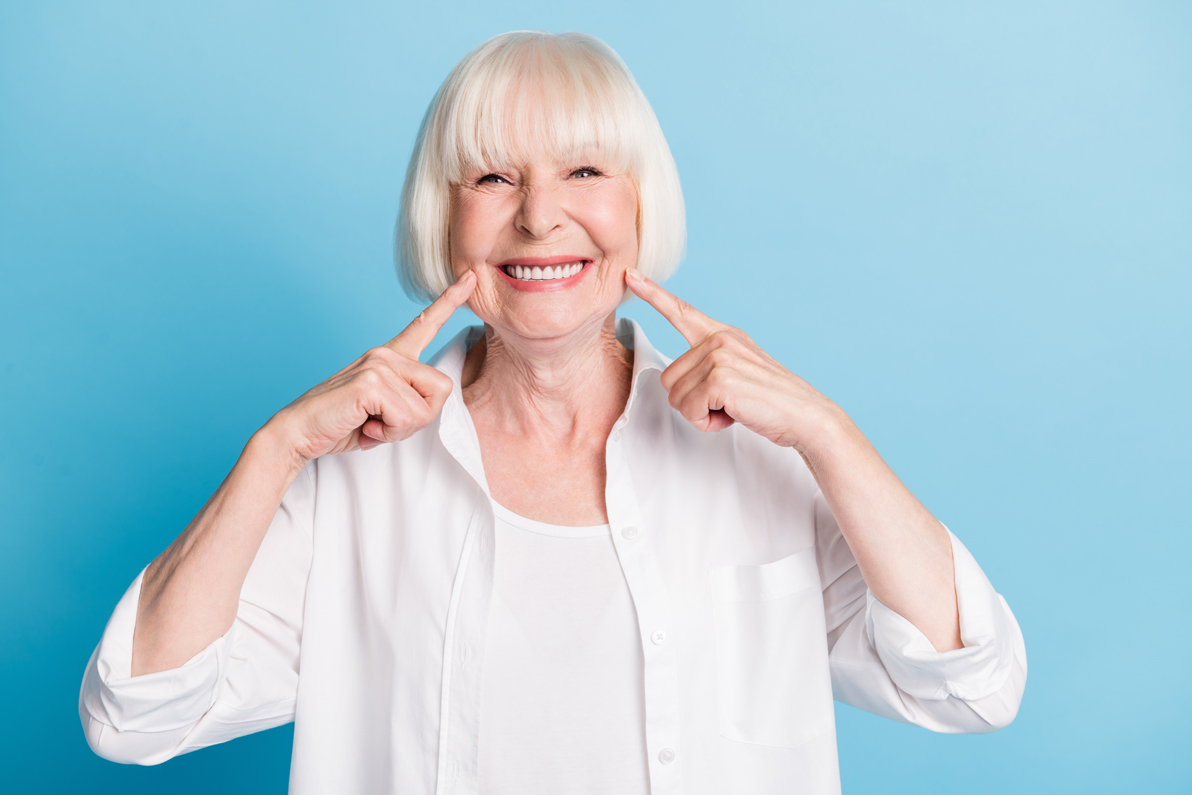 senior woman with short hair in white clothes smiling and pointing to her smile