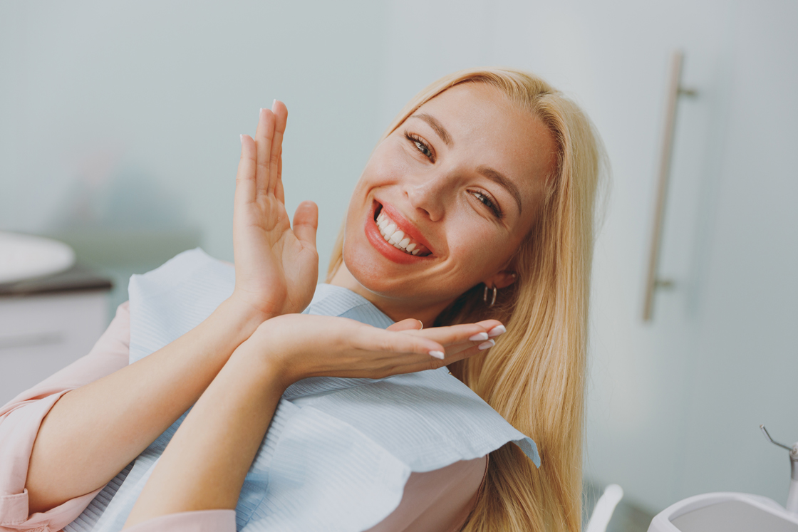 blonde woman in dental chair smiling with hands raised to her face